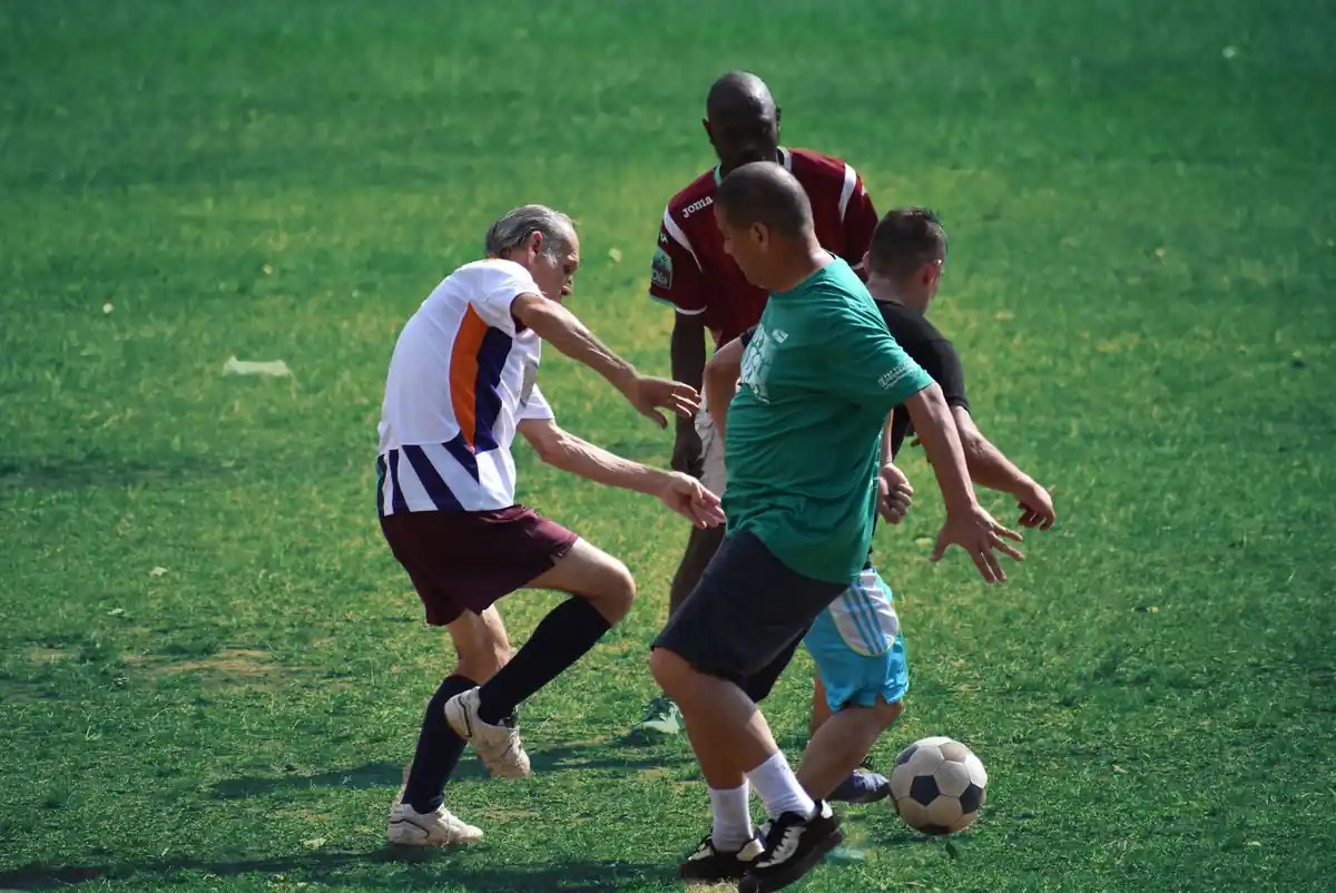 Erwachsene Fußballer in gemischten Teams bei einem Spiel auf dem Rasenplatz.